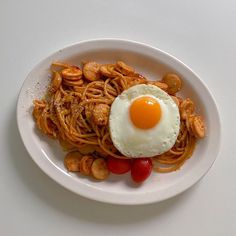 a white plate topped with pasta and an egg on top of it next to cherry tomatoes