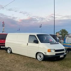 two vans parked next to each other in a field with people standing near them and an rv behind them