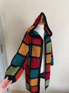 a colorful crocheted jacket hanging on a white wall next to a mannequin