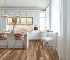 a kitchen with white cabinets and wooden floors, two pink stools in front of the counter