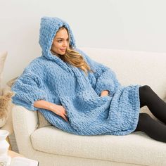 a woman is sitting on a couch wearing a blue blanket and black leggings