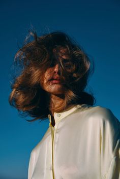 a woman with her hair blowing in the wind on a sunny day, against a blue sky