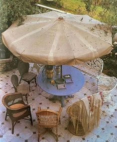 an outdoor table with chairs and umbrella in the middle of a patio area that looks like it has been set up for dinner