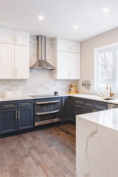 a kitchen with white cabinets and wood flooring is pictured in this image, there is a stainless steel range hood over the stove