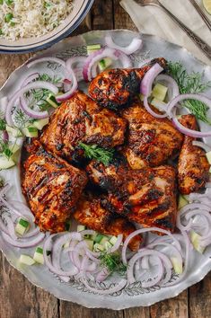 grilled chicken with onions and fennels on a plate next to a bowl of rice