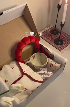 an open box with various items inside on a table next to a candle and other decorations