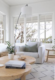 a living room filled with furniture and a table in front of two large white windows