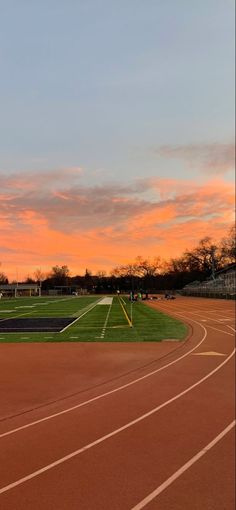 the sun is setting over a track with an athletic field in the foreground and trees in the background