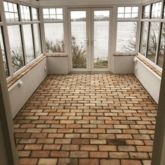 an empty room with brick flooring and large windows overlooking the water from it's side