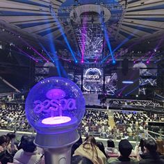 a large room filled with lots of people sitting in front of a stage that has purple and blue lights on it