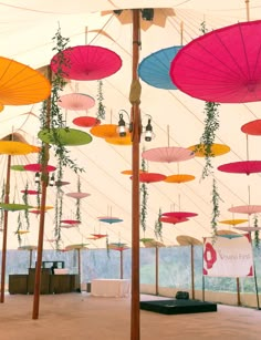 many colorful umbrellas hanging from the ceiling in an open air tent with plants growing out of them