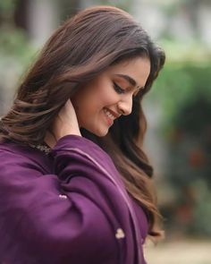 a woman with long hair smiling and touching her ear