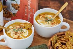 two white bowls filled with soup on top of a wooden table next to crackers