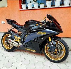 a black and gold motorcycle parked in front of an orange building with potted plants