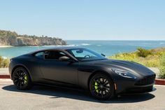 a black sports car is parked on the side of the road near the ocean and cliffs