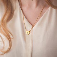 a woman wearing a gold necklace with a heart shaped initial on the front and bottom