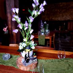 there is a vase with purple flowers in it on the table next to some wine glasses