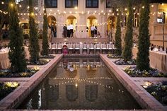 an outdoor wedding venue with tables and chairs around the pool at night, surrounded by greenery