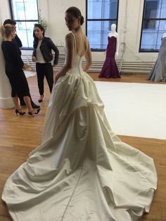 a woman in a wedding dress standing on a wooden floor with other people around her