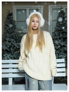 a woman standing in front of a bench wearing a white hat and sweater with long blonde hair