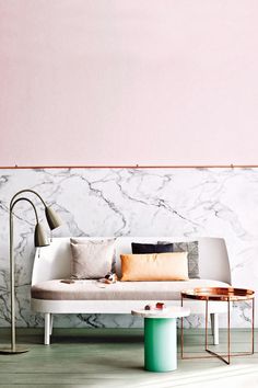 a white couch sitting next to a table on top of a hard wood floor in front of a marble wall