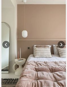 a bed sitting under a mirror next to a white vase and lamp on top of a table