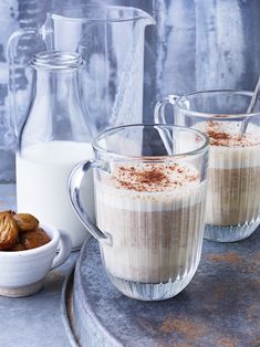 two glasses filled with pudding sitting on top of a table next to milk and nuts