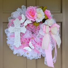 a wreath with pink and white flowers is hanging on the front door as a cross sits next to it