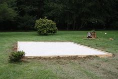 an empty swimming pool in the middle of a grassy area with trees and bushes behind it