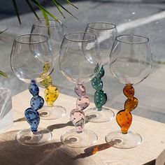 four wine glasses sitting on top of a wooden table next to a potted plant