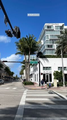 two people crossing the street in front of a tall building with palm trees on both sides