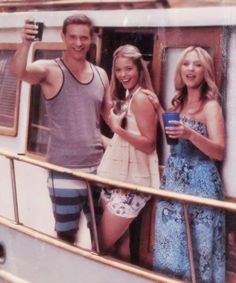 two women and a man are standing on the deck of a boat with their arms in the air