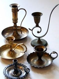 an assortment of antique silver items on a white table top, including candlesticks and saucers