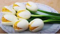 several pieces of hard boiled eggs on a white plate with green onions and spring flowers