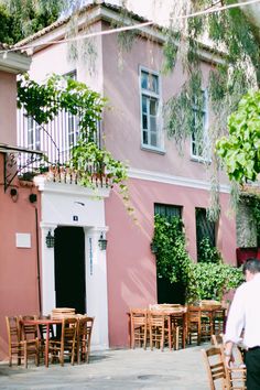 people are sitting at tables in front of a pink building with ivy growing on it