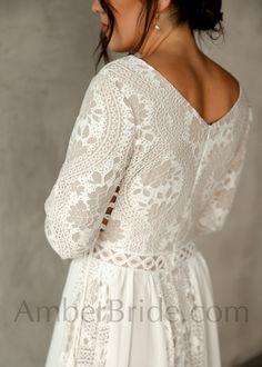 the back of a woman wearing a white dress with long sleeves and an open shoulder