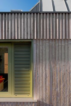 an open window on the side of a building with slatted metal siding and green shutters