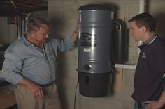 two men standing next to each other in front of a water heater and tank