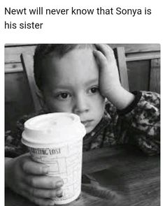 a little boy sitting at a table with a coffee cup in front of his face