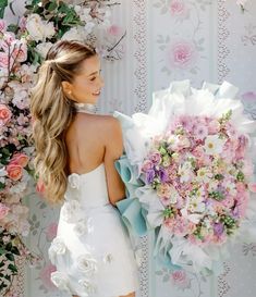 a woman holding a bouquet of flowers in front of a wall with pink and white flowers