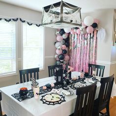 a table set up for a party with balloons and streamers hanging from the ceiling