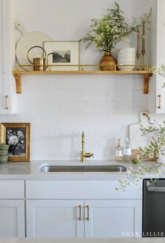 a kitchen with white cabinets and gold trim on the shelves above the sink is filled with flowers