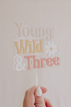 a hand holding a cake topper that says young, wild and three