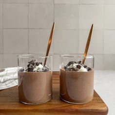 two glasses with ice cream and cookies in them on a wooden tray next to a white tile wall