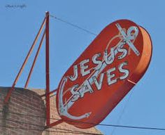 a red sign that says jesus saves hanging from the side of a brick building in front of a blue sky