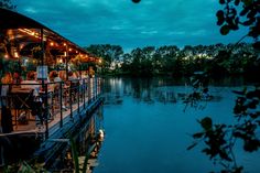 people are sitting at tables on the dock by the water as the sun goes down