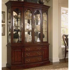 a large wooden china cabinet with glass doors and drawers in a living room area next to a dining room table