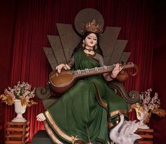 a statue of a woman sitting on a throne with a guitar in her hand and flowers around her