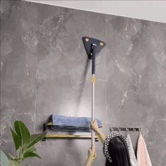 a woman holding a broom in her hand while standing next to a wall mounted towel rack