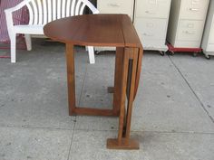 a wooden table sitting on top of a sidewalk next to white chairs and filing cabinets